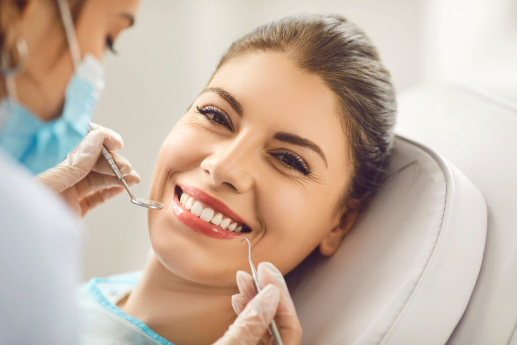 Young beautiful woman smiling at a dentist appointment, face close-up. The doctor holds dental instruments near the girls face. Concept of beautiful teeth and smile, tooth whitening